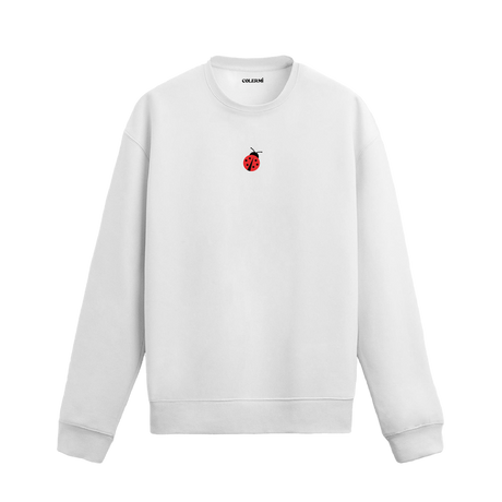 Beyaz sweatshirt üzerinde göğüs kısmında kırmızı küçük uğur böceği baskısı bulunan minimal tasarım.
