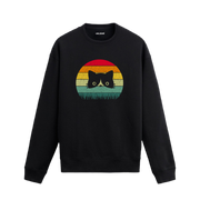 Siyah sweatshirt üzerinde retro gün batımı renklerinde çimenlerin arasından bakan kedi baskısı