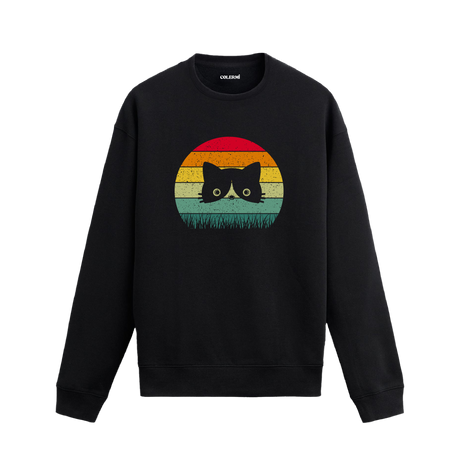 Siyah sweatshirt üzerinde retro gün batımı renklerinde çimenlerin arasından bakan kedi baskısı