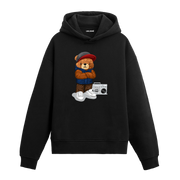 Kollarını göğsünde birleştirmiş, şapkalı ve müzik çaları yanında duran şehir tarzı ayıcık baskılı hoodie tasarımı.