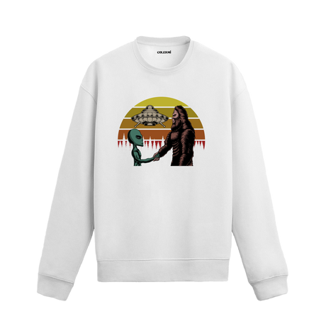 Uzay temalı beyaz sweatshirt üzerinde uzaylı ve kocaayak figürlerinin el sıkıştığı, arkada UFO ve retro güneş tasarımı bulunan yaratıcı illüstrasyon.